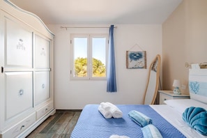 Ein Schlafzimmer mit Bett, Kleiderschrank, einem Fenster mit Vorhängen, einem Nachttisch mit Lampe und einer Wanddekoration.