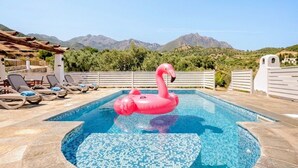 A swimming pool with a pink flamingo float, lounge chairs, and a mountainous backdrop. - Vacation home with sea view Ogliastra Sardinia Casa Lentisco D (Foxi Murdegu)