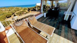 A balcony with a view of the sea, a wooden deck, and a covered seating area. - Vacation home with sea view Ogliastra Sardinia Casa Lentisco D (Foxi Murdegu)