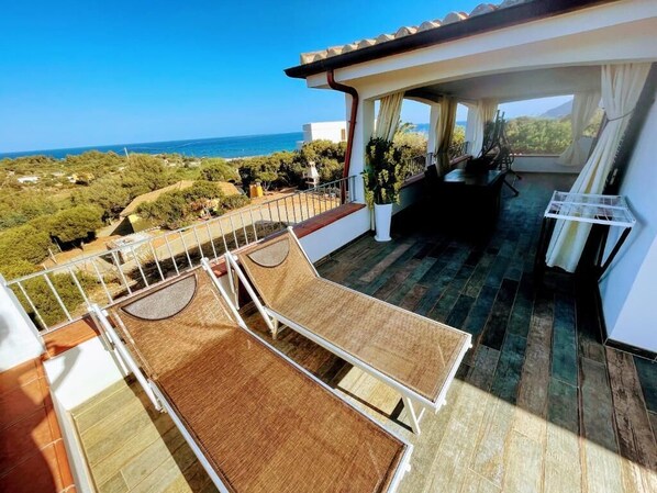 Un balcón con vistas al mar, una terraza de madera y una zona de estar cubierta.