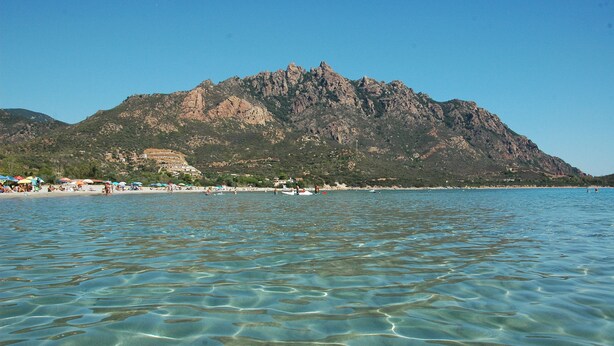 A beach with clear water, a mountain in the background, and beach umbrellas. - Vacation home with sea view Ogliastra Sardinia Casa Lentisco D (Foxi Murdegu)