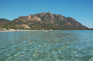 Una playa con aguas cristalinas, una montaña al fondo y sombrillas de playa.