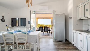 A modern kitchen with white cabinets, a dining area with a table set for four, and a view of the outdoors. - Vacation home with sea view Ogliastra Sardinia Casa Lentisco D (Foxi Murdegu)