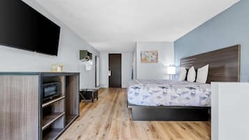 A modern hotel room with a bed, a flat-screen TV, a microwave, and a desk with a lamp.