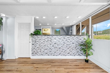 A hotel reception area with a modern design, featuring a reception desk, a logo, and a view of the outdoors.