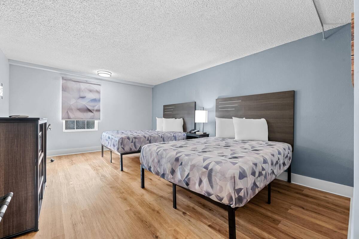 A hotel room with two beds, a desk, and a window.