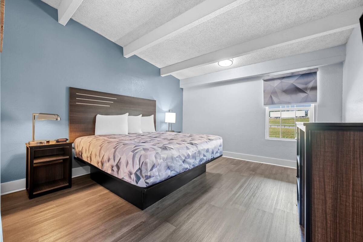 A bedroom with a bed, nightstand, lamp, and window with blinds.
