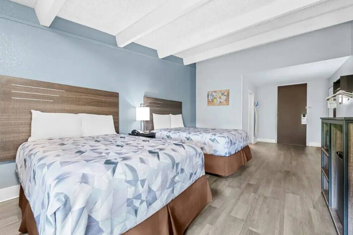 A hotel room with two beds, a wooden headboard, a desk, and a cabinet.
