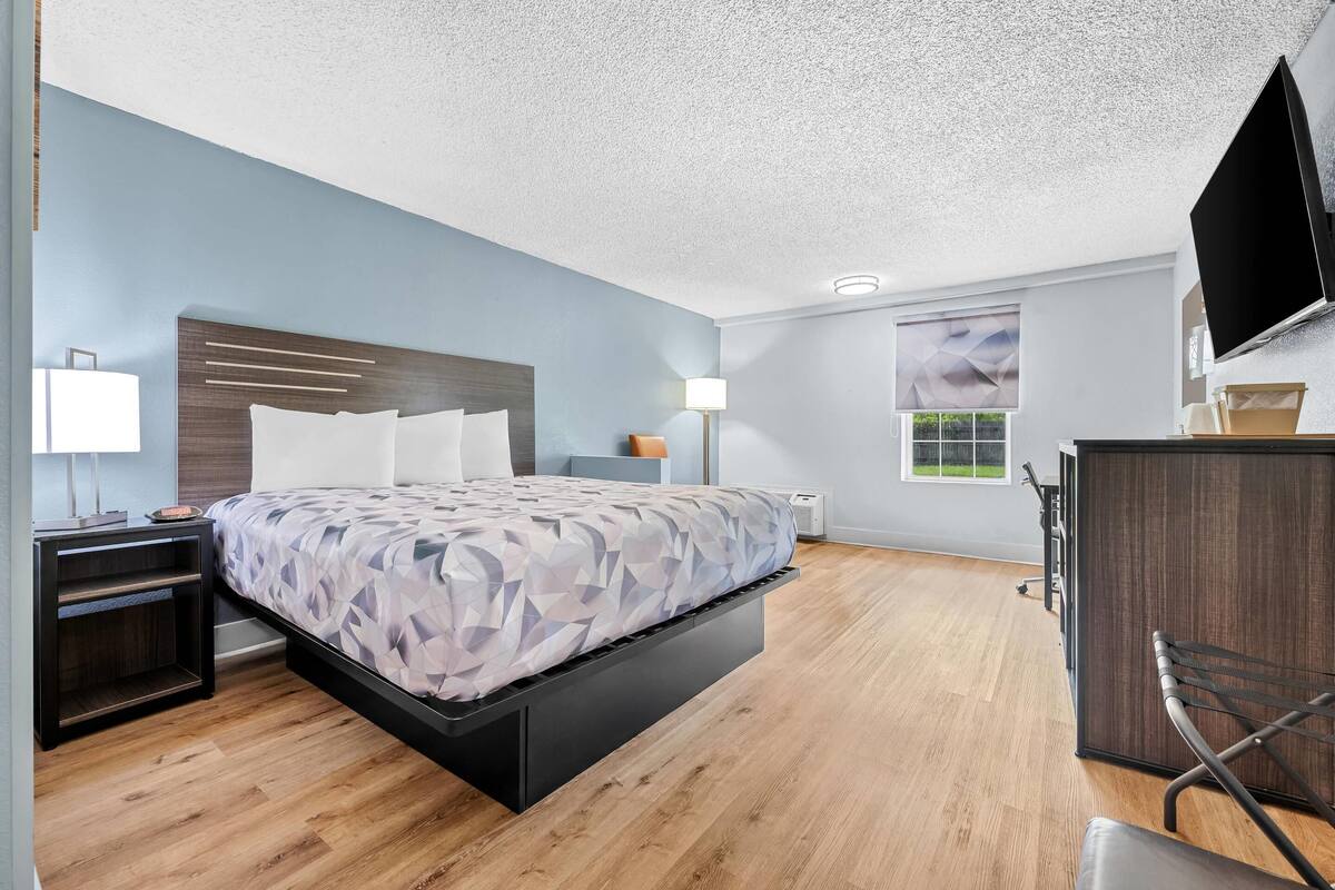 A modern bedroom with a bed, bedside tables, a desk, a chair, and a TV.