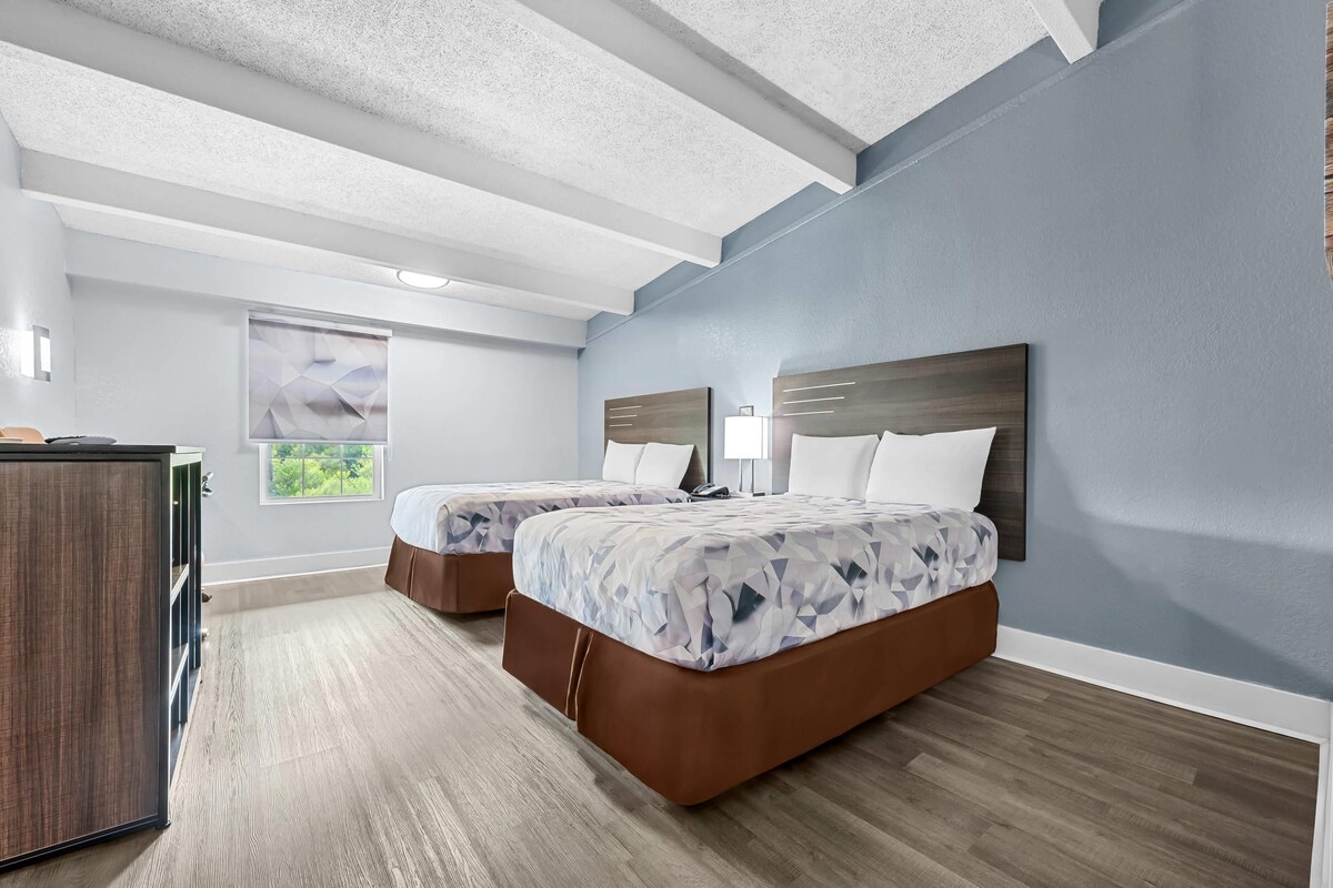 Un dormitorio moderno con dos camas, un aparador de madera y un ventanal grande.