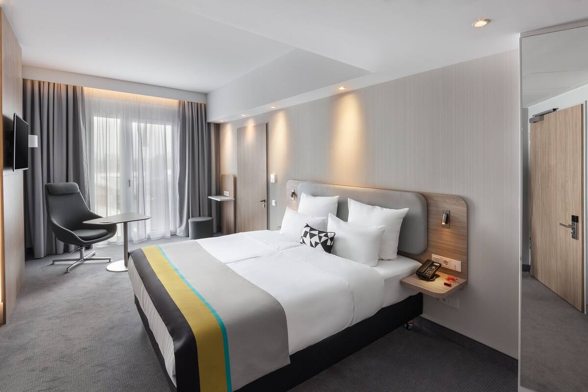 Ein modernes Hotelzimmer mit einem großen Bett, einem Schreibtisch, einem Sessel und einem Fernseher.