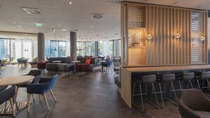 A modern cafe with a bar area, seating arrangements, and large windows providing natural light. - Holiday Inn Express Düsseldorf – Hauptbahnhof by IHG (Düsseldorf)