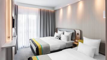 Habitación de hotel con dos camas, un escritorio y un ventanal con cortinas translúcidas.
