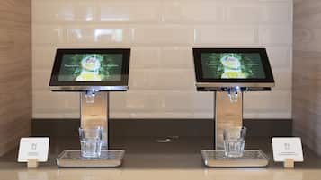 Two self-service juice dispensers with digital screens, each with a glass and a card holder for payment.