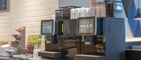 A coffee machine with a digital display, stacked paper cups, and a menu board.