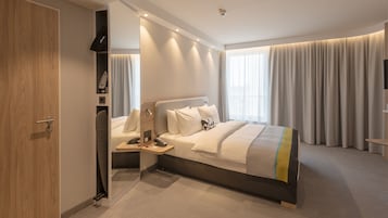 Una camera d'hotel moderna con un letto grande, un comodino, una TV integrata e un armadio.
