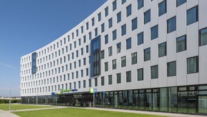 A modern hotel building with a flat facade, large windows, and a green sign indicating it is a Holiday Inn Express. - Holiday Inn Express Düsseldorf – Hauptbahnhof by IHG (Düsseldorf)