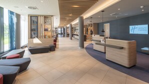 A modern hotel lobby with a reception desk, seating areas, and a view of the outdoors. - Holiday Inn Express Düsseldorf – Hauptbahnhof by IHG (Düsseldorf)