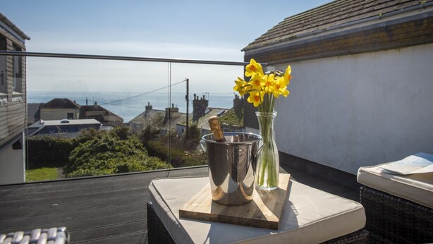 Een balkon met uitzicht op zee, een vaas met gele bloemen en een champagnefles.