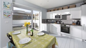 Een moderne keuken met witte kastjes, een eettafel gedekt voor twee personen en uitzicht op buiten via een glazen deur.