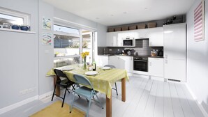 Een moderne keuken met witte kasten, een eettafel met stoelen en een raam met uitzicht op een tuin.