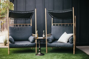 Un canapé deux places doté d’un auvent, une petite table ronde avec deux bouteilles, et un coussin à motifs.