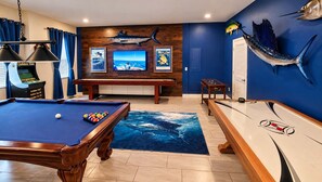 A pool table with a blue ocean-themed rug, a billiards table, and a mounted fish sculpture.