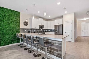 A modern kitchen with a green wall, bar stools, and stainless steel appliances.