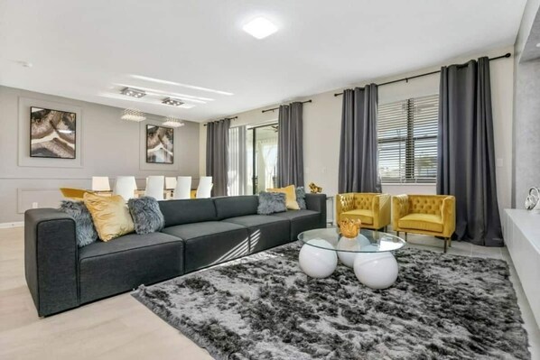 Een moderne woonkamer met een bank, fauteuils, een glazen salontafel en een groot vloerkleed.