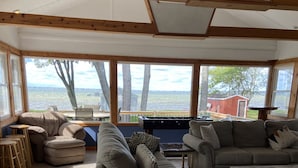 Ein geräumiges Wohnzimmer mit großen Fenstern und Blick auf ein Gewässer, ausgestattet mit Sofas und einem Kicker.