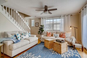 A living room with a staircase, a ceiling fan, a sofa set, a coffee table, and a floor lamp.
