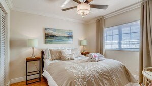 A bedroom with a bed, two bedside tables, a ceiling fan, a painting, and a window with blinds. - Spacious and Charming 2 level beach condo (Lauderdale-by-the-Sea)