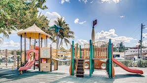 A playground with slides and climbing structures, surrounded by palm trees and a clear sky. - Spacious and Charming 2 level beach condo (Lauderdale-by-the-Sea)