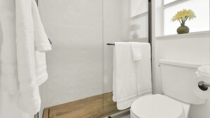 Un baño moderno con cabina de ducha de vidrio, un inodoro blanco y un mueble de tocador de madera.