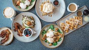A breakfast spread with various dishes including waffles, bacon, eggs, and a salad.