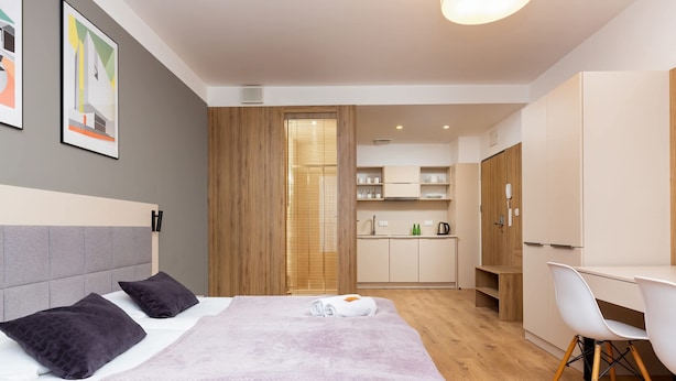 A modern hotel room with a bed, a desk, and a kitchenette.