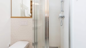 A modern bathroom with a glass-enclosed shower, a toilet, and a mirror with a wooden frame.