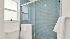 A bathroom with a glass shower enclosure, a white toilet, and a window with a vase of reed sticks.