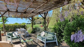 An outdoor seating area with a pergola, two green cushioned sofas, a wooden chair, and a small table with a bowl and a decorative item. - Bella Valle 3 Campagna, Relax in Giardino, Mare a 2 km e la Toscana Tuta Intorno (Toscana)