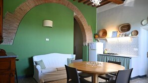 A cozy room with a green wall, a white sofa, a wooden dining table with chairs, and a kitchen area with a stove and shelves. - Bella Valle 3 Campagna, Relax in Giardino, Mare a 2 km e la Toscana Tuta Intorno (Toscana)