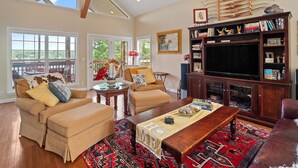 A spacious living room with a large TV, comfortable seating, a bookshelf, and a view through the windows. - Blue Door - Entertainment area downstairs with a pool table (Arley)