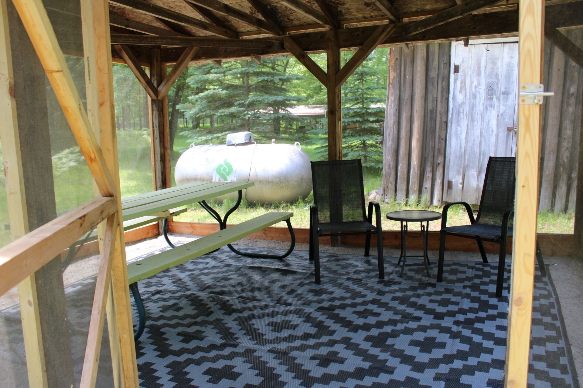A covered outdoor seating area with a picnic table, two chairs, and a grill.