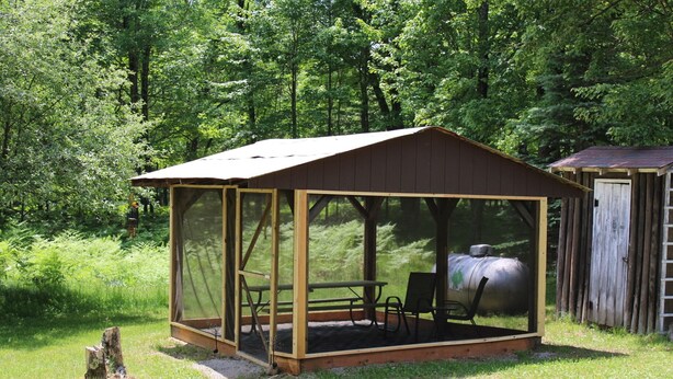 A covered outdoor seating area with a table and chairs, surrounded by a wooden fence and a metal tank. - Book your SUMMER FUN now - lakes, waterfalls, ATV/UTV trails! Your fun awaits! (Crivitz)