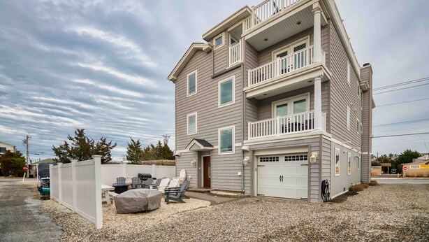 A two-story house with a garage, a covered patio with chairs, and a fenced yard. - Beachside 8BR • 1 Block from Ocean (Surf City)
