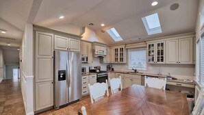 A spacious kitchen with white cabinetry, a large wooden dining table, and a skylight. - Beachside 8BR • 1 Block from Ocean (Surf City)