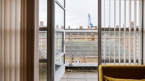Une pièce dotée d’une grande fenêtre donnant sur un paysage urbain, avec une rambarde en métal et un canapé jaune.