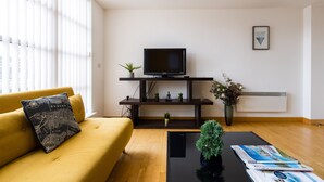 Un salon moderne avec un canapé jaune, un meuble de rangement noir et un téléviseur à écran plat.