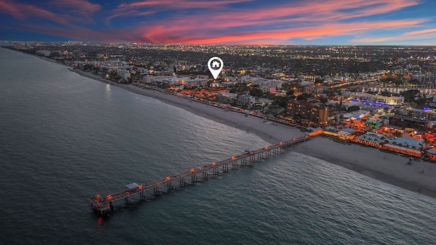 Vista aérea de uma cidade costeira com um longo píer que se estende para o mar, uma praia e uma área urbana densamente povoada com edifícios iluminados.