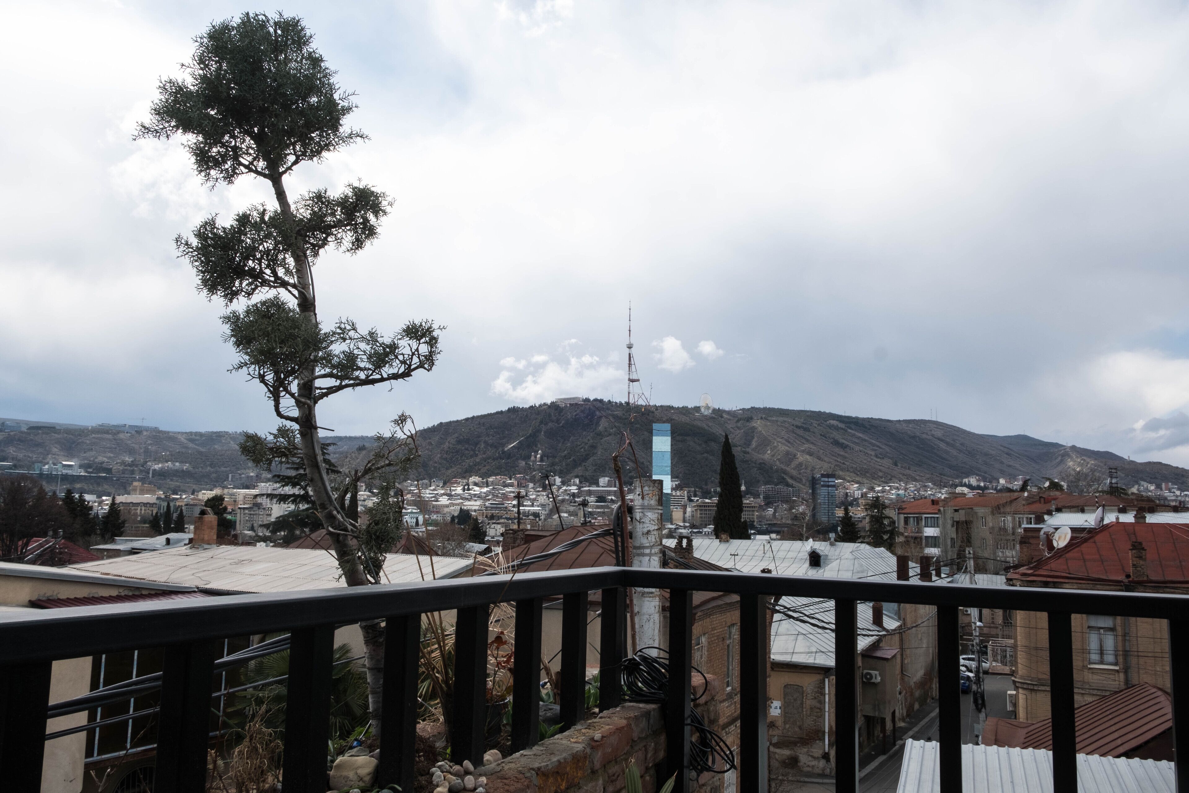 Un balcón con vistas a un paisaje urbano, que incluye edificios y una montaña al fondo.