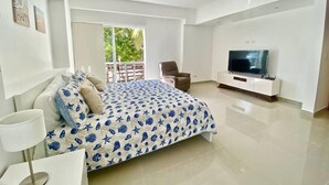 A modern bedroom with a bed, a TV, a ceiling fan, and a balcony with a view of greenery. - Cap Cana PentHouse w/ terrace & private pool (Punta Cana)